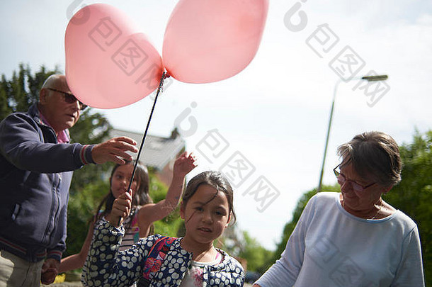 祖父母和他们的孙女在街上散步，孙女在她的生日那天举着一个心形的大气球