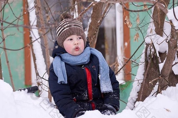冬天，一个男孩戴着针织帽子，戴着围巾在雪地里玩耍。