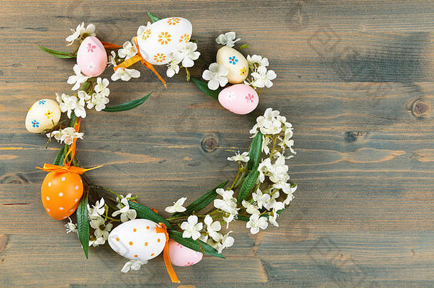五颜六色的复活节彩蛋和春天的鲜花组成的花环。在质朴的木制背景上。