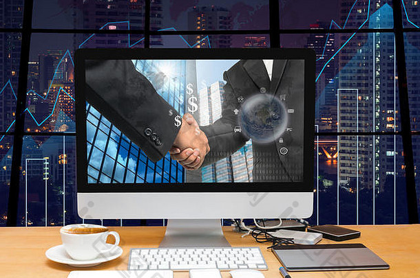 工作区，电脑桌面，商人在交易图上的屏幕上握手，模糊的城市景观背景照片，