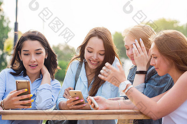 一群年轻的<strong>女生</strong>坐在公园的桌子旁，面带微笑地讨论着拿着智能手机的东西。<strong>聊天</strong>、互联网、技术
