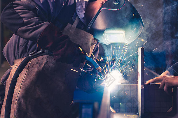 在大会堂焊接金属型材的带焊和防护头盔的工业焊工