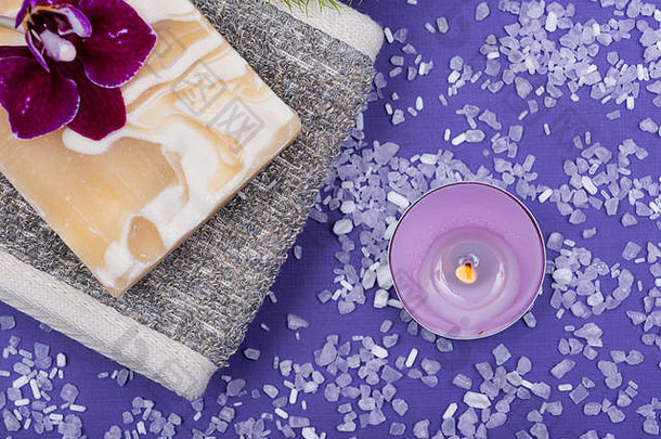 Spa健康概念。天然的背部洗涤器，羊奶皂，玄武岩石头，兰花，竹子和薰衣草茶蜡烛，紫色背景。