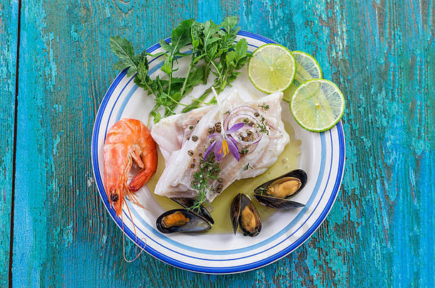 鳕鱼片、大西洋鳕鱼配海鲜贻贝、虾、酸橙和蔬菜，蓝色木质背景