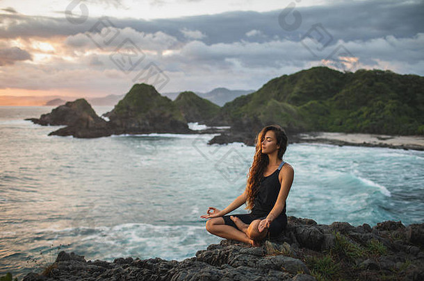 年轻女子在日落时以莲花姿势练习瑜伽，欣赏美丽的海景和山景。对自然的敏感。自我分析和自我反省。s