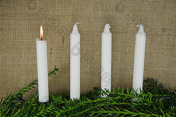 四支降临节蜡烛，其中一支在粗麻布背景下燃烧