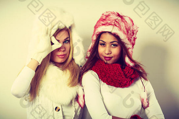 时尚<strong>冬季服装</strong>概念。两个金发女孩和黑白混血儿穿着温暖的红白衣服，玩得很开心。穿着毛皮帽子、围巾、手套的漂亮女人。