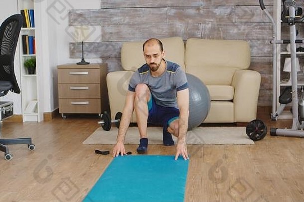 这名男子穿着运动服在客厅里展开<strong>瑜伽垫</strong>。