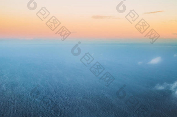 冬季日落日出时飞机在海面上高空飞行的鸟瞰图。晴朗晴朗的黎明天空，<strong>冷暖色</strong>调。