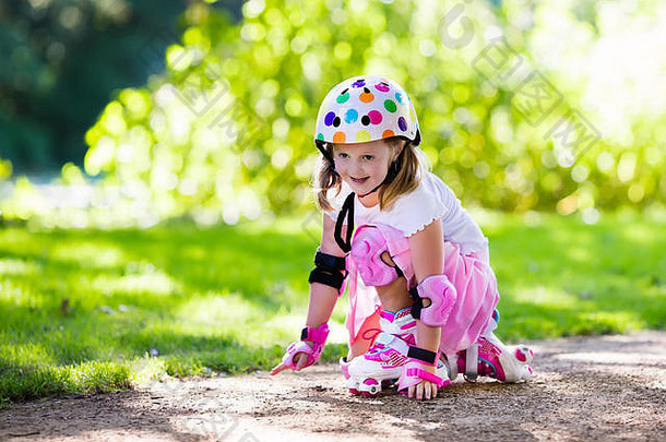 在阳光明媚的夏季公园里<strong>学习</strong>溜冰的小女孩。儿童佩戴护肘和护膝、护腕和安全帽，以确保安全
