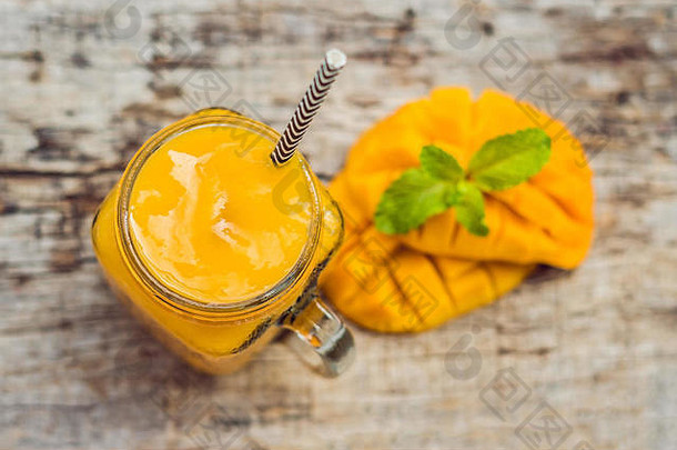 芒果冰沙装在玻璃罐里，芒果放在绿色背景上。芒果奶昔。热带水果概念。