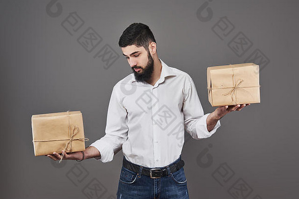 英俊浪漫的男人看着盒子，做出了选择。拿着一个灰色背景的两个<strong>大礼</strong>盒<strong>送</strong>给他的夫妇。