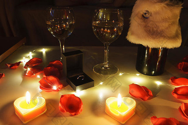 近距离观看浪漫的餐桌，桌上有葡萄酒、玫瑰、蜡烛和订婚戒指