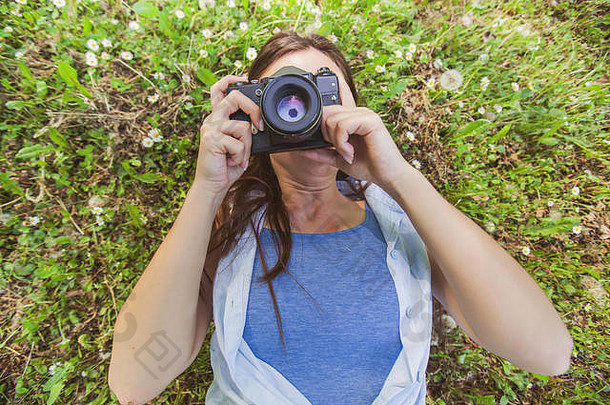 年轻的业余女摄影师躺在地上，用老式相机在大自然中拍照