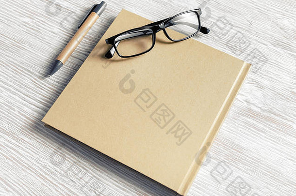 封闭式空白方形笔记本、眼镜和笔，背景为浅色木质桌子。