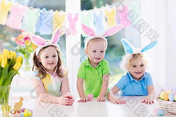 复活节早晨，男孩和女孩在早餐时戴着兔子耳朵，坐在桌子旁，手里拿着复活节彩蛋篮。孩子们庆祝复活节。