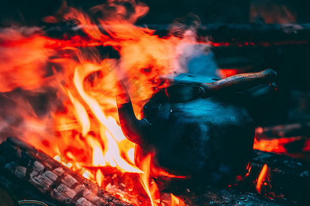 古老的复古铁制营地水壶在森林里的火上<strong>烧开</strong>水。黄昏之夜篝火的明火