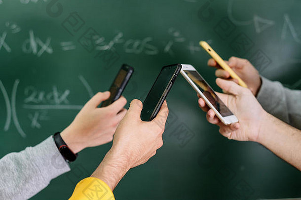 学生在教室里使用手机，背景是黑板。