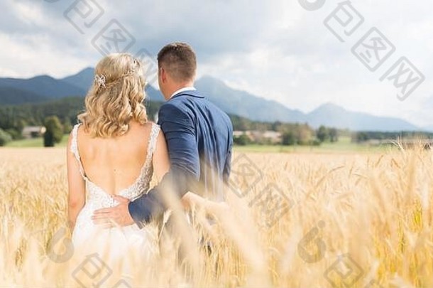 在斯洛文尼亚农村的麦田里，新郎温柔地拥抱新娘的后视图。
