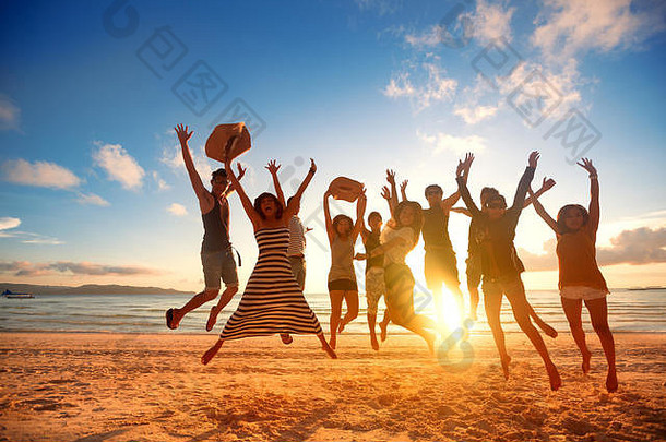 一群快乐的年轻人在美丽的夏日夕阳下在海滩上跳跃