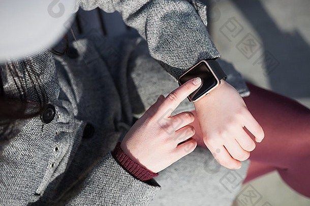 穿着灰色外套和marsala紧身裤的女士使用她时髦的智能手表。此人<strong>始终</strong>连接到社交媒体和互联网。