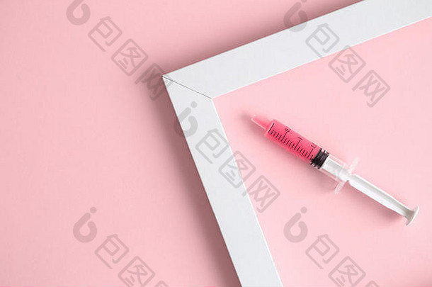 注射器和相框的平面布置在柔和的粉红色背景上，这是一个最小的创意概念。