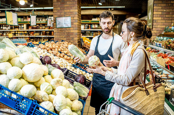店员在超市帮助年轻女顾客挑选蔬菜
