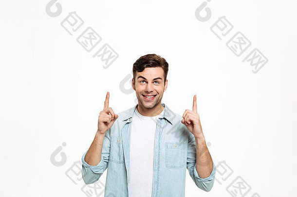 一个快乐的年轻人站在白色背景上，用两个手指向上指着的肖像