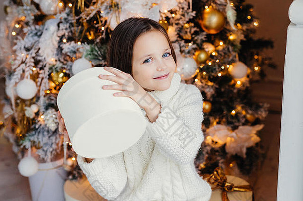蓝眼睛漂亮<strong>可爱</strong>的小孩拿着礼物盒，想知道里面是什么，站在新年或圣诞树附近，从父母那里得到惊喜。