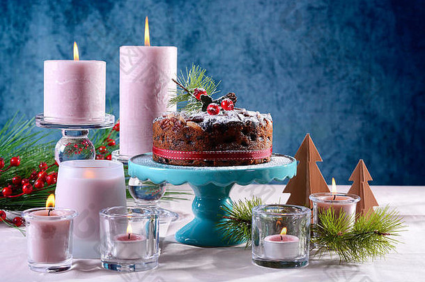 节日假期表格英语风格<strong>圣诞节</strong>水果蛋糕迷人的表格设置粉红色的蜡烛蓝色的背景复制空间