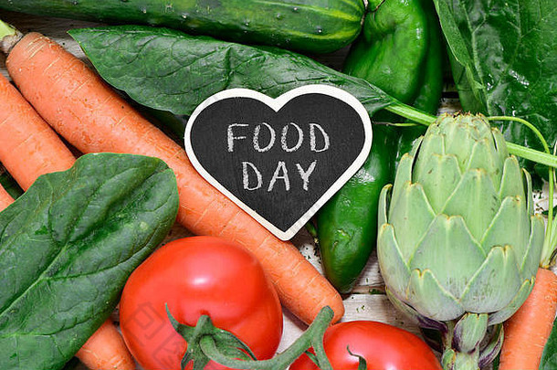 在一堆不同的生蔬菜上，比如黄瓜，放上一块热形黑板的特写，上面写着“食物日”，