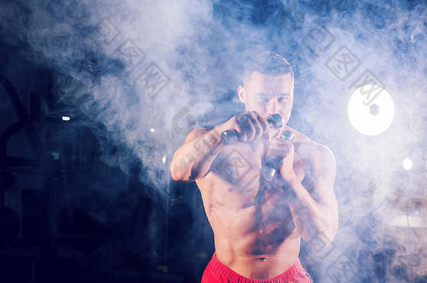 强壮的男子做拳击练习，用哑铃直击。运动型肌肉男的照片。力量和动力