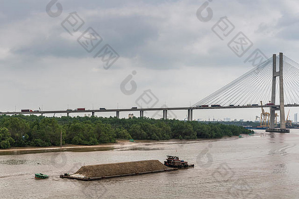 越南胡志明市——2019年3月12日：宋西贡河。短拖船用沙子推长驳船。我的桥在后面。棕色的水，绿色的b