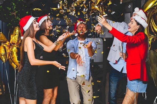 一起庆祝新年。一群戴着圣诞帽的漂亮年轻人扔着五颜六色的彩纸，看起来很开心。