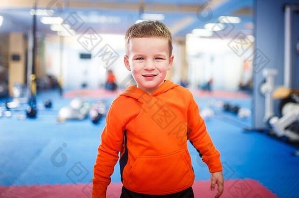 一个孩子在健身房摆姿势的肖像。主题是儿童的身体发育。一个穿着运动服的运动员正在看摄像机。童年和