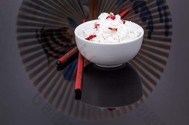 碗煮熟的白色大米新装的可食用的玫瑰花瓣