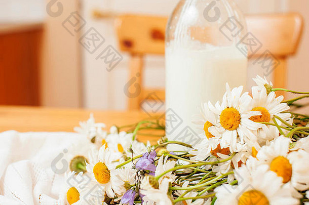 简单时尚的木制厨房，桌上放着一瓶牛奶和玻璃，夏天的花朵甘菊，健康的早晨食品概念