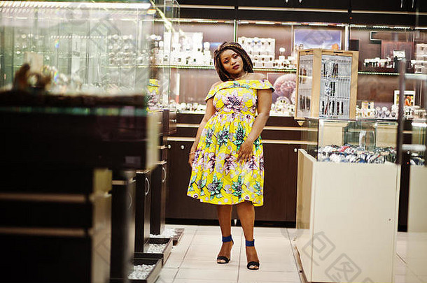 可爱的身材矮小的非洲裔美国女孩，留着可怕的长发，在购物中心的手表店里穿黄色的衣服。