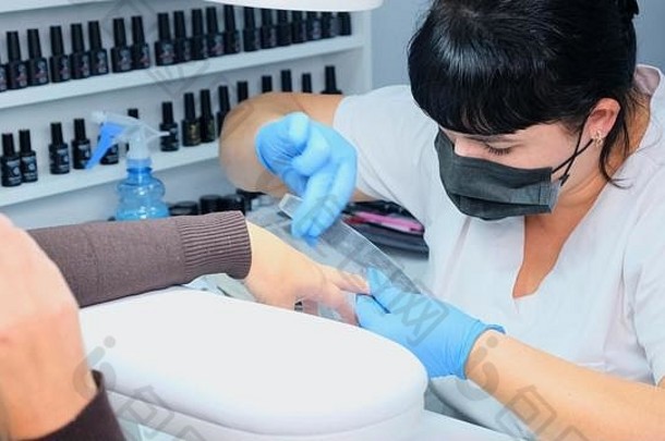 特写镜头：一名妇女在美甲沙龙接受美容师用指甲锉修指甲。女人正在修指甲。美容师锉指甲