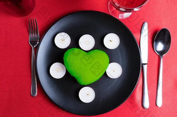情人节那天盘子上的心和蜡烛。优雅的餐厅餐具。潘通绿色主题。浪漫的餐桌布置。