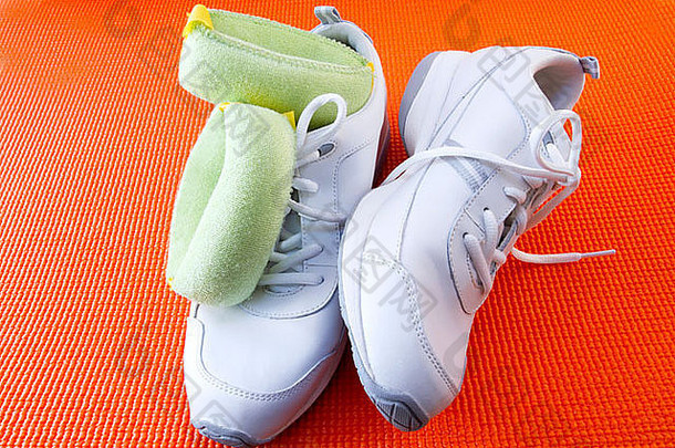 橙色瑜伽垫上白色运动鞋和浅绿色腕带配重的特写镜头，反映出运动和健身的准备状态。