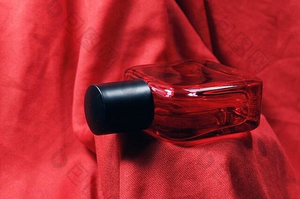 红色男士香水瓶，以红色丝绸为背景。红色香水瓶，黑色瓶盖，自然喷雾。