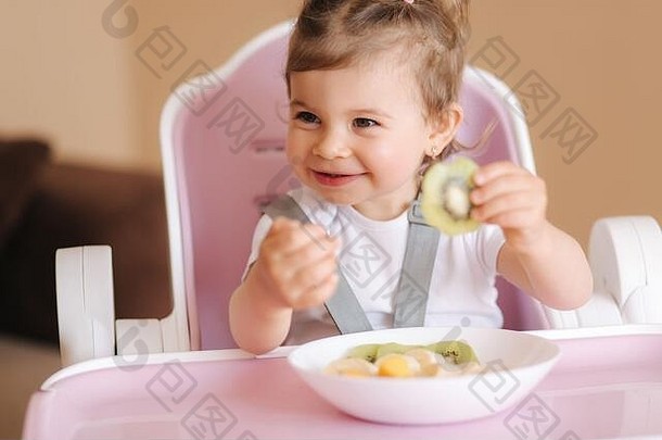 快乐的小孩在高椅子上吃猕猴桃的画像。儿童健康营养