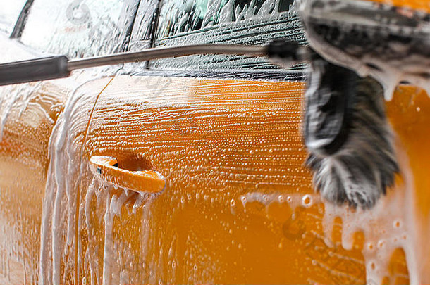 深黄色洗车机洗车侧的细节。刷子在白色肥皂和洗发水泡沫中留下笔触。