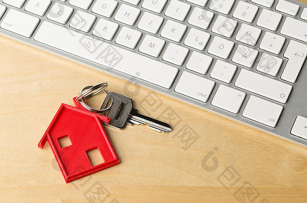 带有红色<strong>房屋</strong>钥匙链挂件和木制桌上的电脑键盘的<strong>房屋</strong>门钥匙-在线<strong>房屋租赁</strong>或购买概念