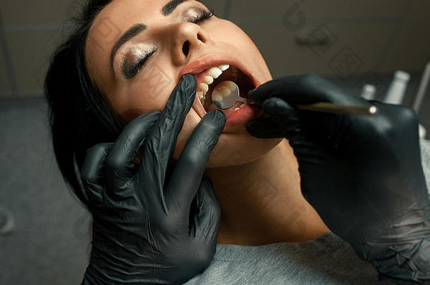 牙医医生用镜子检查年轻女子的牙齿。牙医接待病人。闭合。
