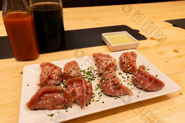 在亚洲餐厅或中国酒吧的木桌上放着两瓶酱油和红辣椒，还有红肉、虾和蘑菇饺子