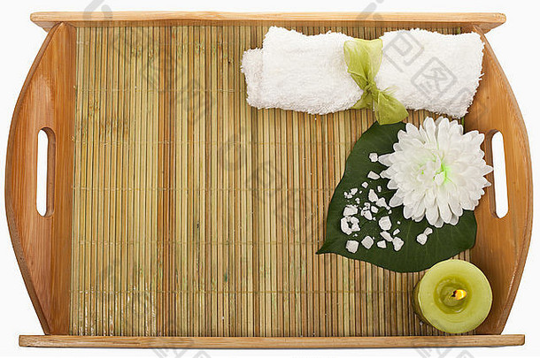以卷毛巾和绿色蜡烛为水疗背景，托盘上有海盐叶子和白色花朵。