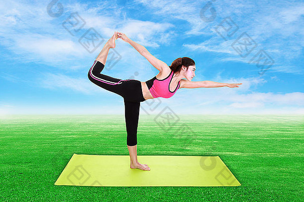 年轻女子在绿草蓝天上用瑜伽垫做瑜伽运动