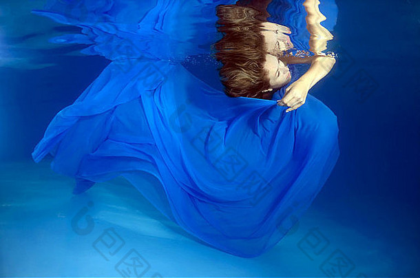 一个留着大头发的年轻女子在水下的游泳池里摆姿势
